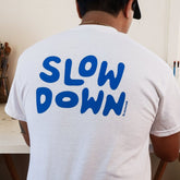 back of white slow-down t-shirt with blue screen printed "slow down" text across upper back